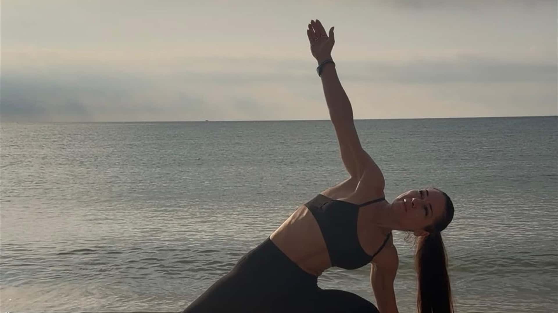 Practică de yoga pe plajă, la răsărit, cu marea în fundal