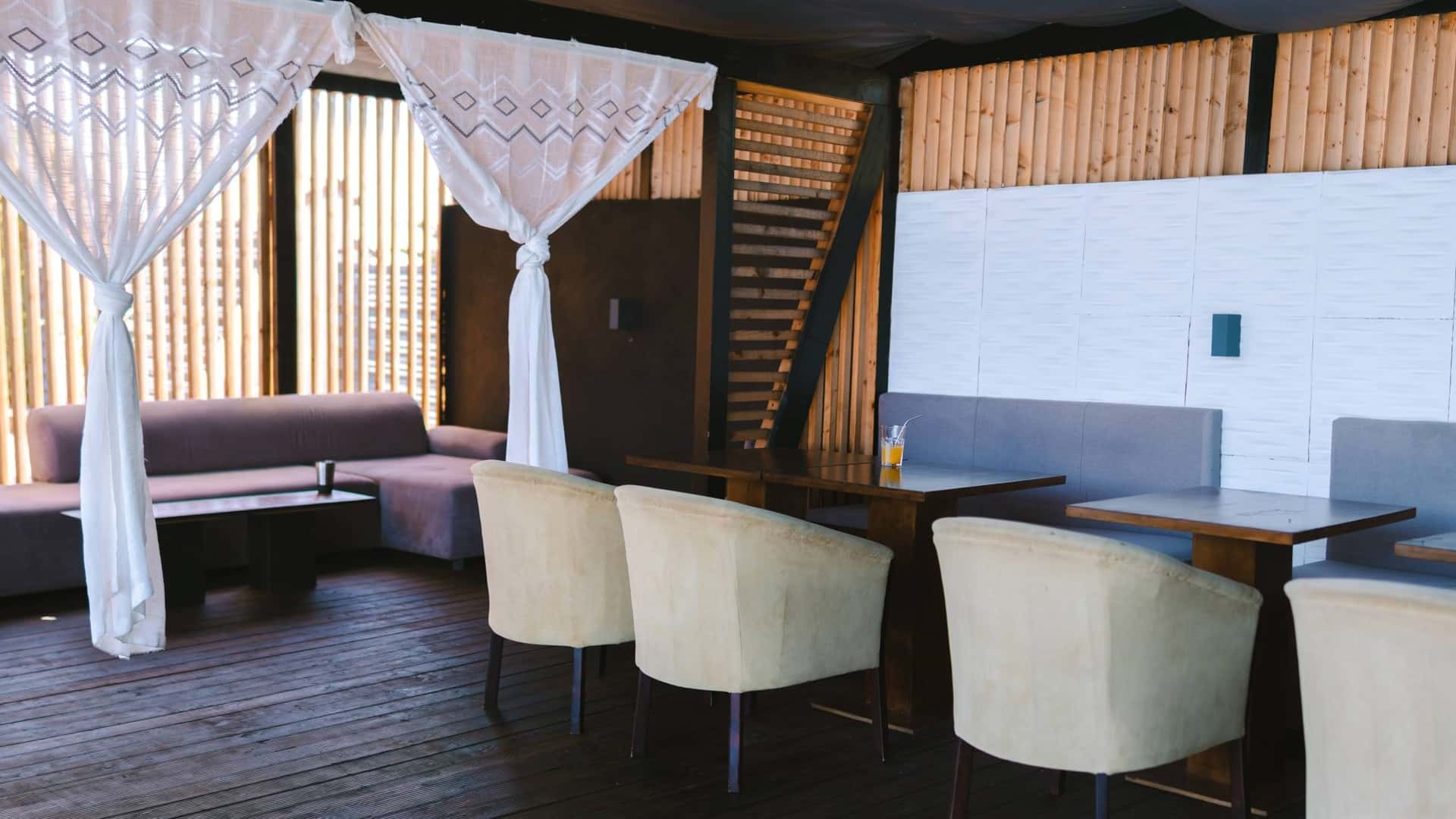 Lounge-ul de pe terasa locației — canapele, perdele albe și lemn cald